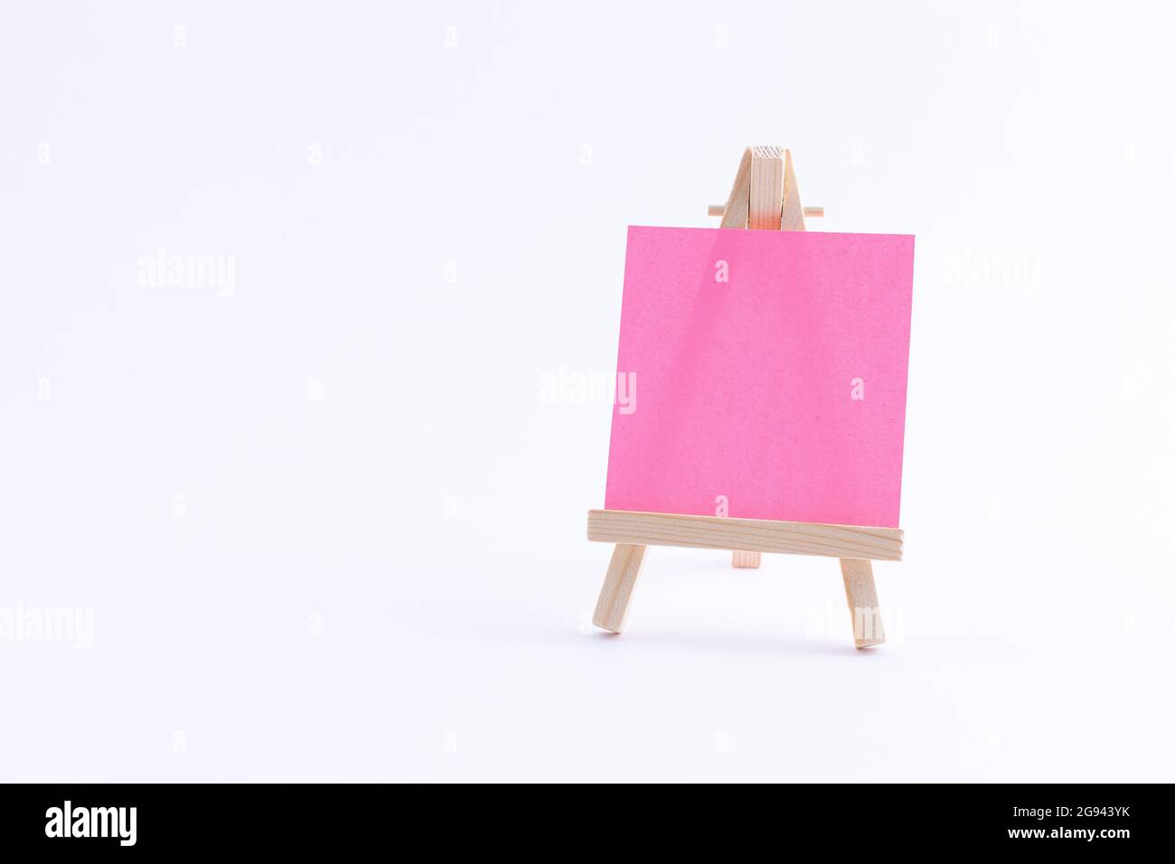 Easel in legno in miniatura con tela quadrata colorata vuota o carta Memo - Mockup. Mini supporto in legno con tavola da disegno pulita su sfondo bianco, spazio per la copia Foto Stock