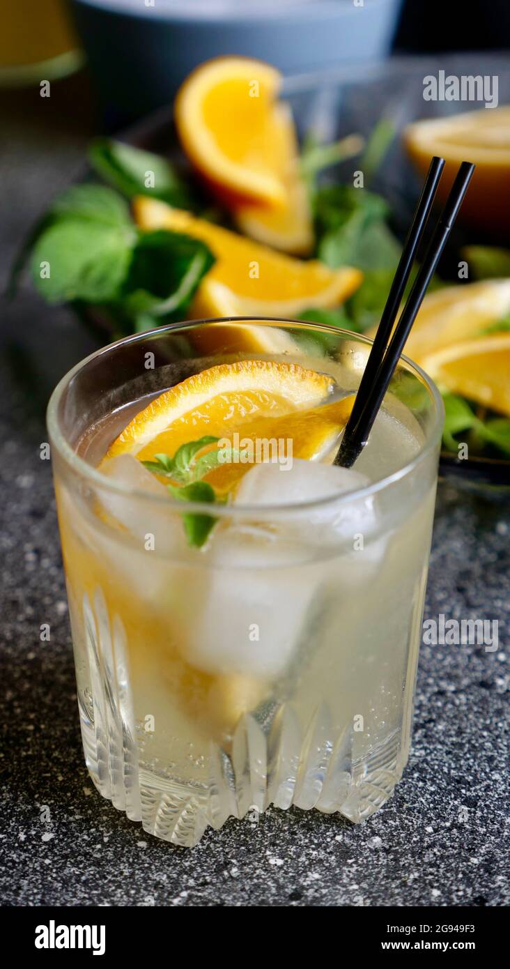 Limonata di limone con menta e ghiaccio in un bicchiere con tubi di plastica neri su fondo di frutta. Rinfrescante bevanda estiva. Primo piano verticale Foto Stock