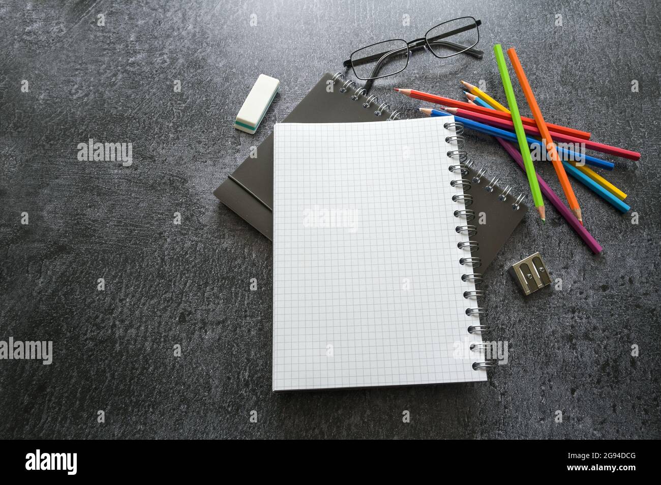 Scrivania da ufficio creativa con notebook a spirale, matite colorate, occhiali e materiali di consumo su un tavolo grigio scuro, spazio per la copia, messa a fuoco selezionata, d stretta Foto Stock