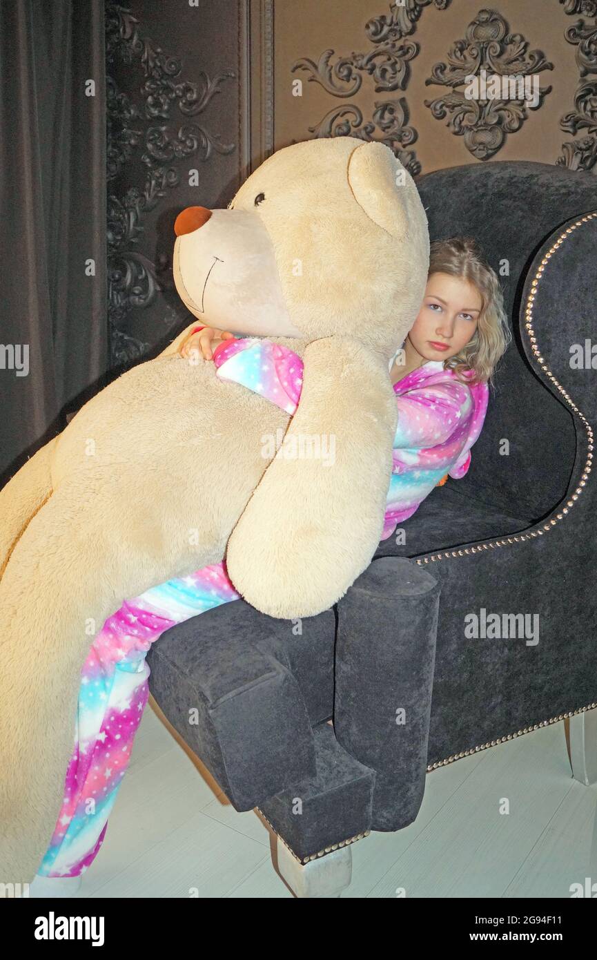 Una ragazza adolescente con un grande orso è seduta su una sedia Foto Stock