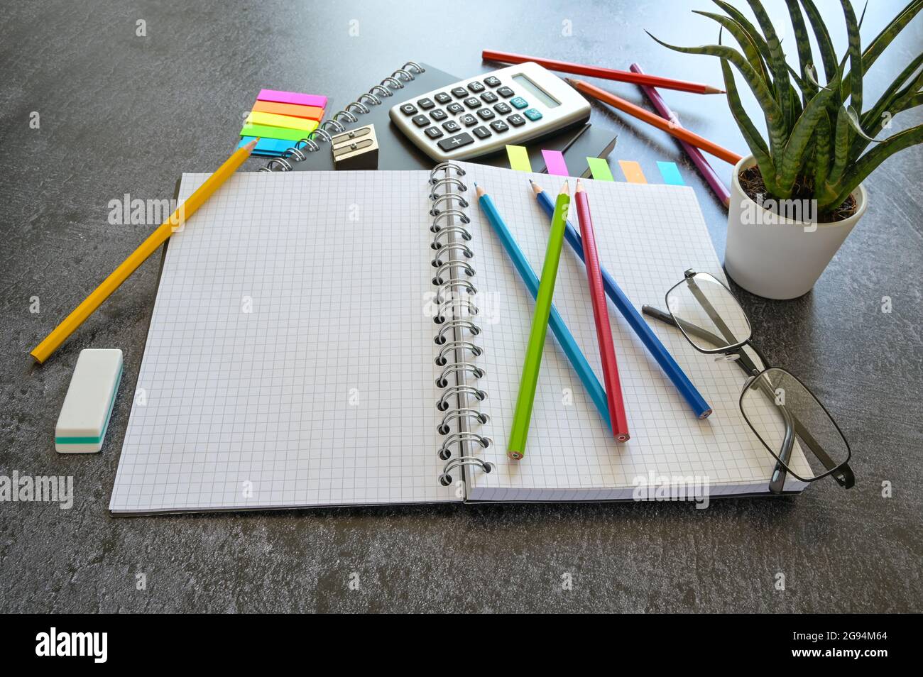 Scrivania da ufficio o studio con un notebook a spirale aperta, matite colorate, calcolatrice e materiale fisso su un tavolo grigio scuro, spazio per la copia, focu selezionato Foto Stock