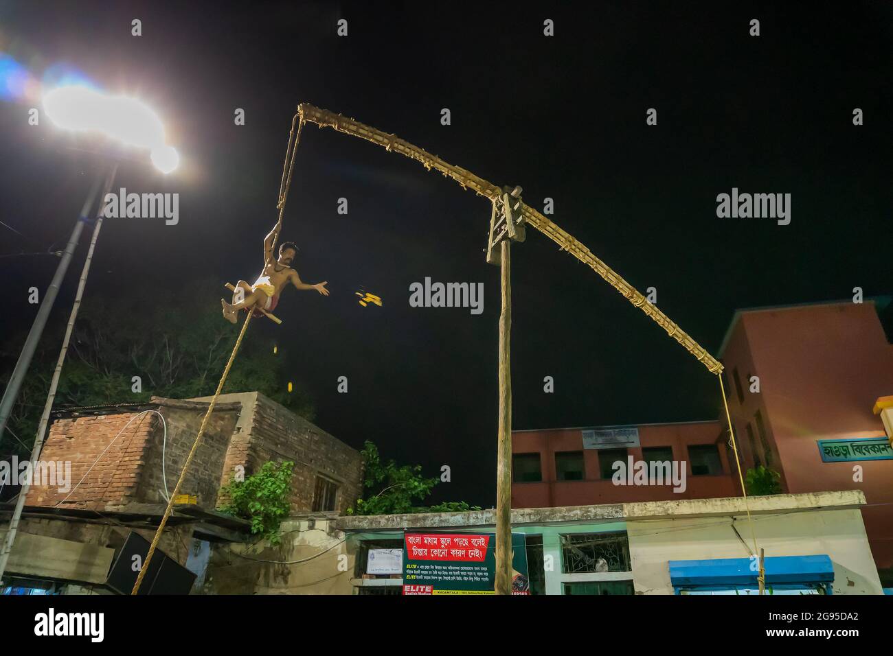 Howrah, Bengala Occidentale, India - 15th Aprile 2019: Il devoto Indù lancia dolci ai devoti mentre pende dal palo in aria, di notte. Sport religiosi. Foto Stock