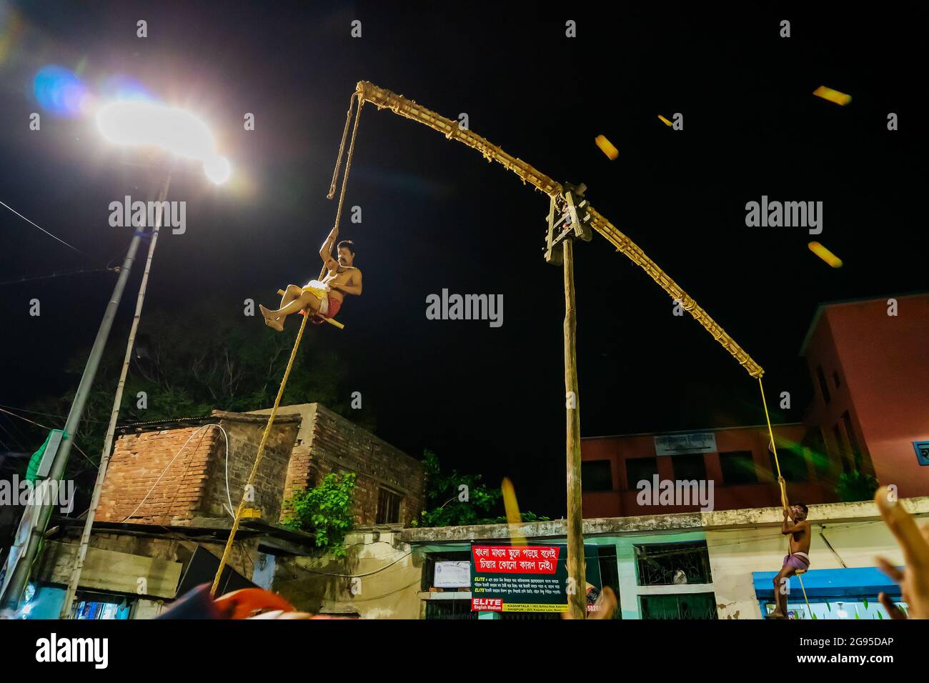 Howrah, Bengala Occidentale, India - 15th Aprile 2019: Il devoto Indù lancia dolci ai devoti mentre pende dal palo in aria, di notte. Sport religiosi. Foto Stock