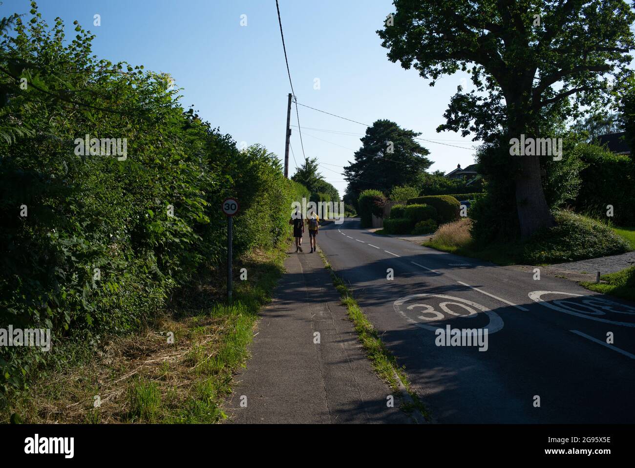 Due ragazzi adolescenti che camminano lungo una tranquilla strada di campagna villaggio con 30 mph segnaletica stradale. L'immagine mostra vivere uno stile di vita rurale per gli adolescenti. Foto Stock