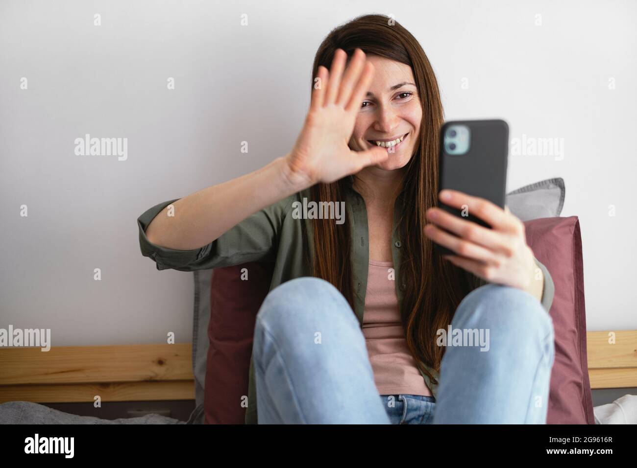 Una giovane donna sorridente che sventolava la mano agli amici durante la videochiamata. Comunicazione online. La vita a casa. Foto Stock