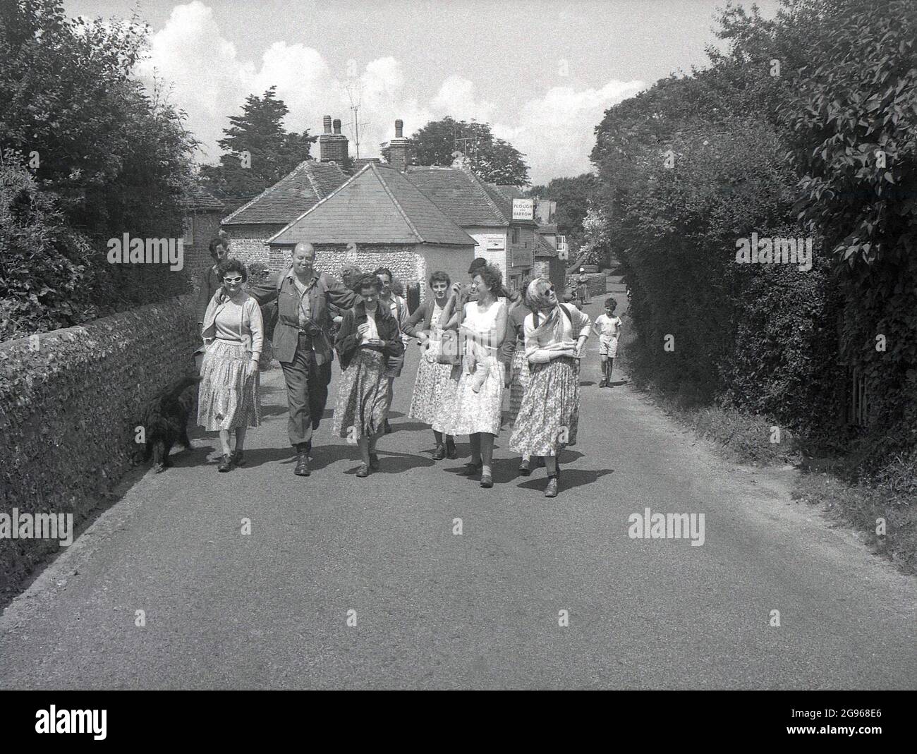 1950s, storico, un gruppo di ramblers, camminando su una corsia fuori del Plow and Harrow Pub a Litlington, Polegate, East Sussex, Inghilterra, Regno Unito, le donne che indossano le lunghe gonne dell'epoca. Un piccolo villaggio o villaggio sulle South Downs, è famoso per il suo grande gesso 'Cavallo Bianco', scolpito sul lato di Hindover Hill, noto come il Cavallo Bianco di Litlington. Foto Stock