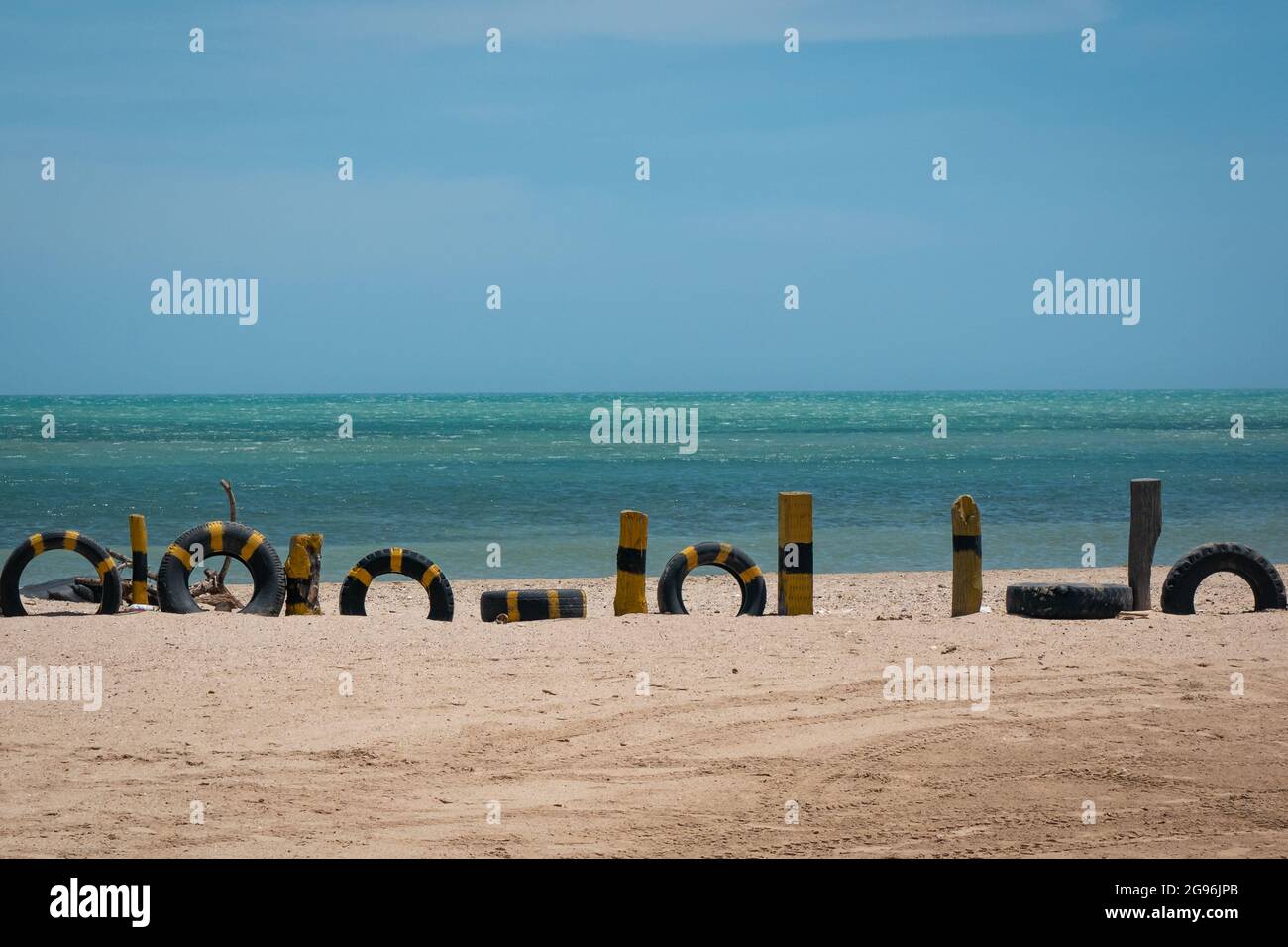 Sfondo del mare alla spiaggia con una recinzione fatta di bastoncini di legno verniciati giallo e pneumatici Foto Stock