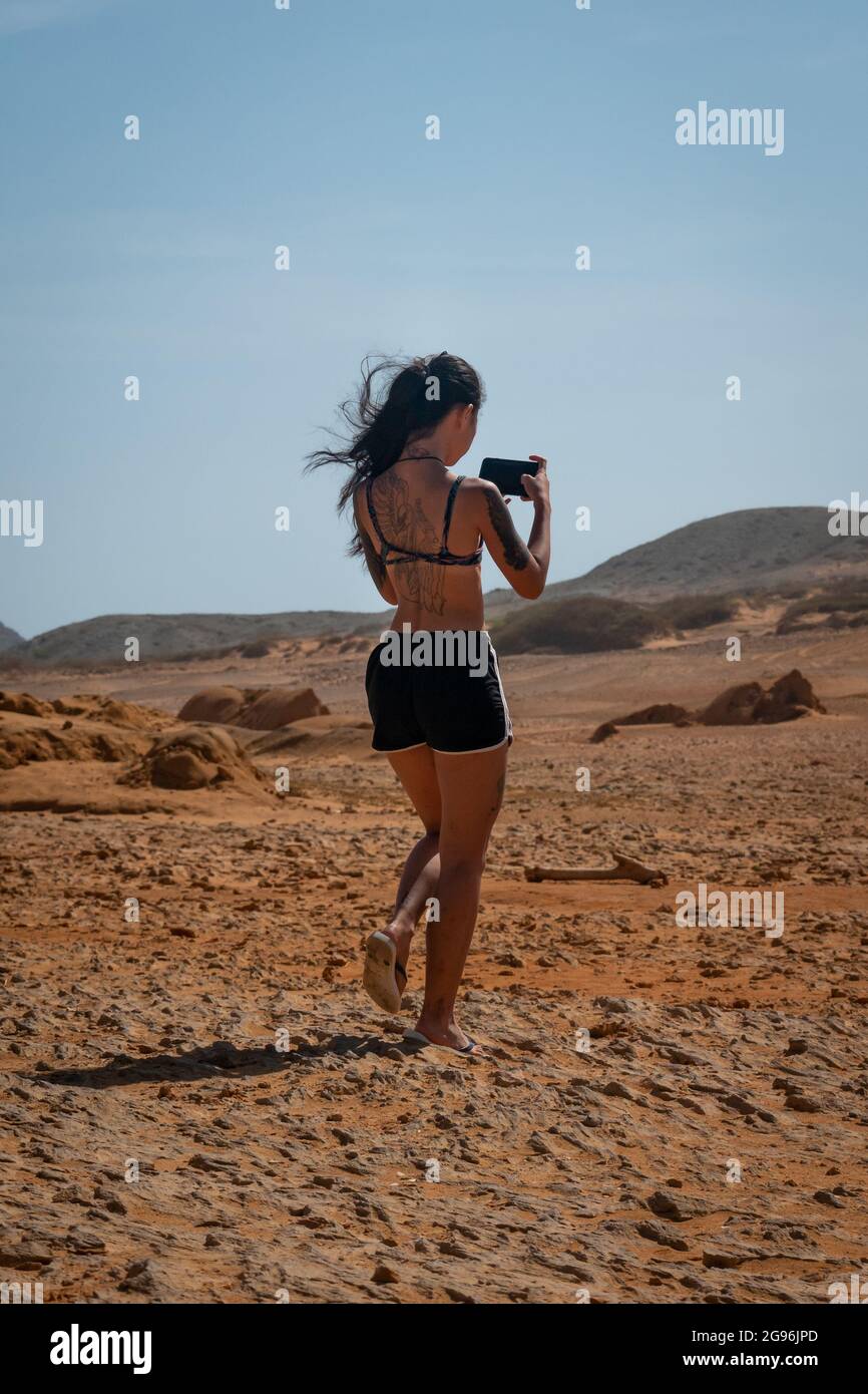 Uribia, la Guajira, Colombia - Maggio 28 2021: Giovane donna asiatica cammina guardando il suo telefono nel deserto Foto Stock