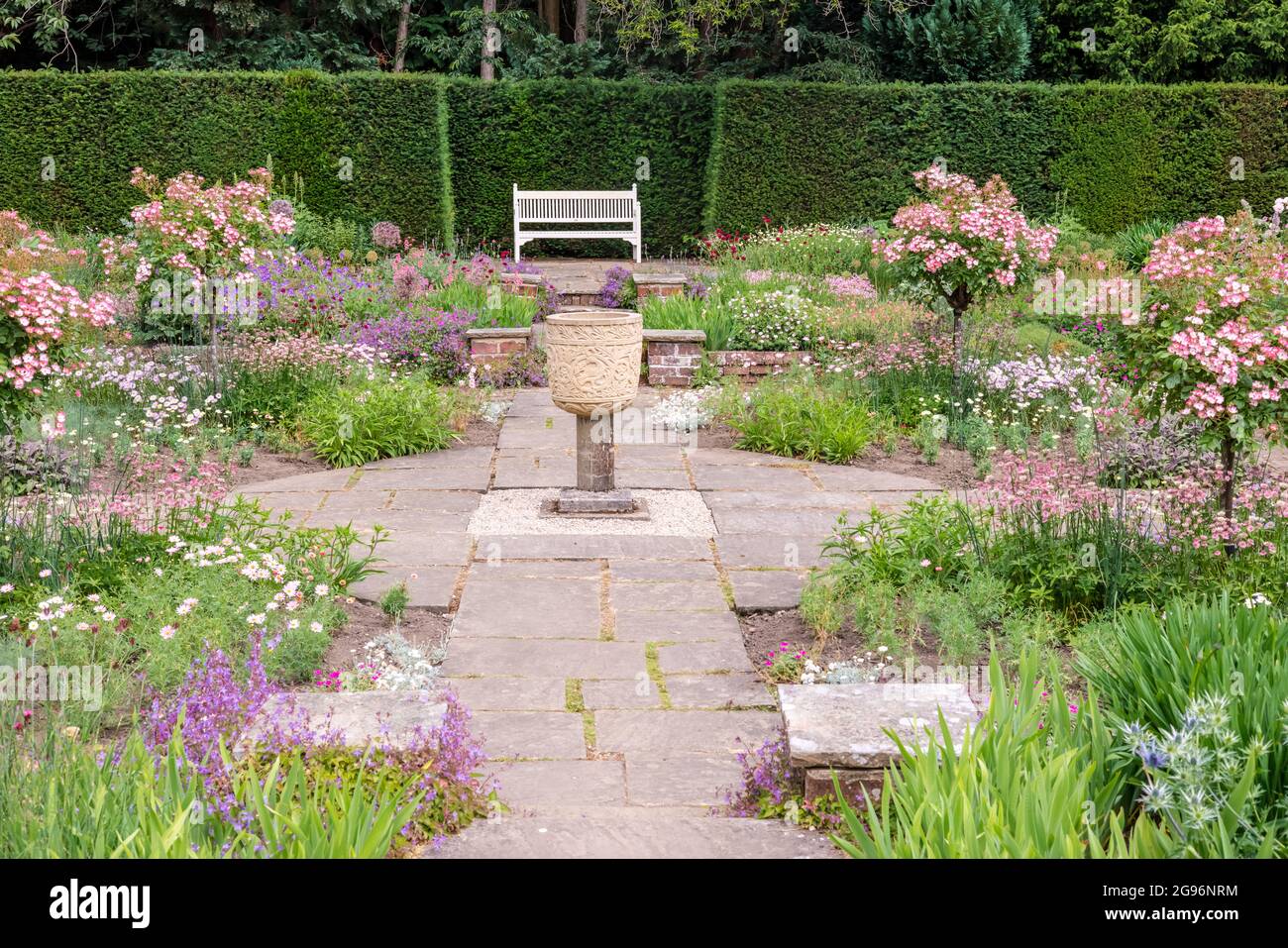 Angolo tranquillo di un giardino inglese segnalato formale con letti di fiori e un vaso di pietra. Foto Stock