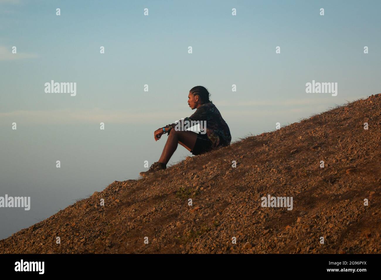Uribia, la Guajira, Colombia - 28 2021 maggio: Giovane uomo marrone latino con le trecce sulla sua testa si siede in attesa del tramonto nel deserto Foto Stock