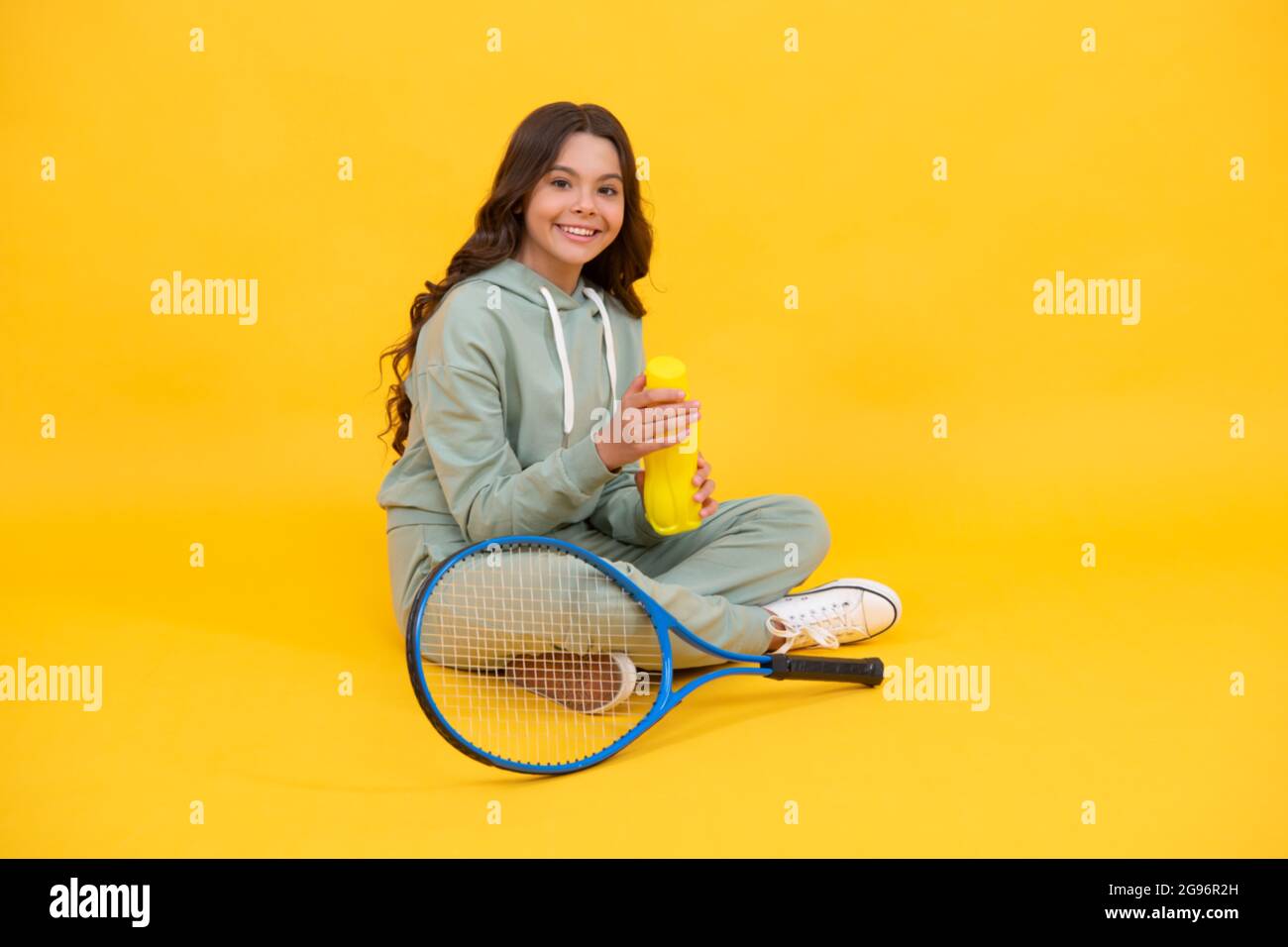happy kid tenere racchetta da tennis e bere acqua da bottiglia su sfondo giallo, idratazione. Foto Stock