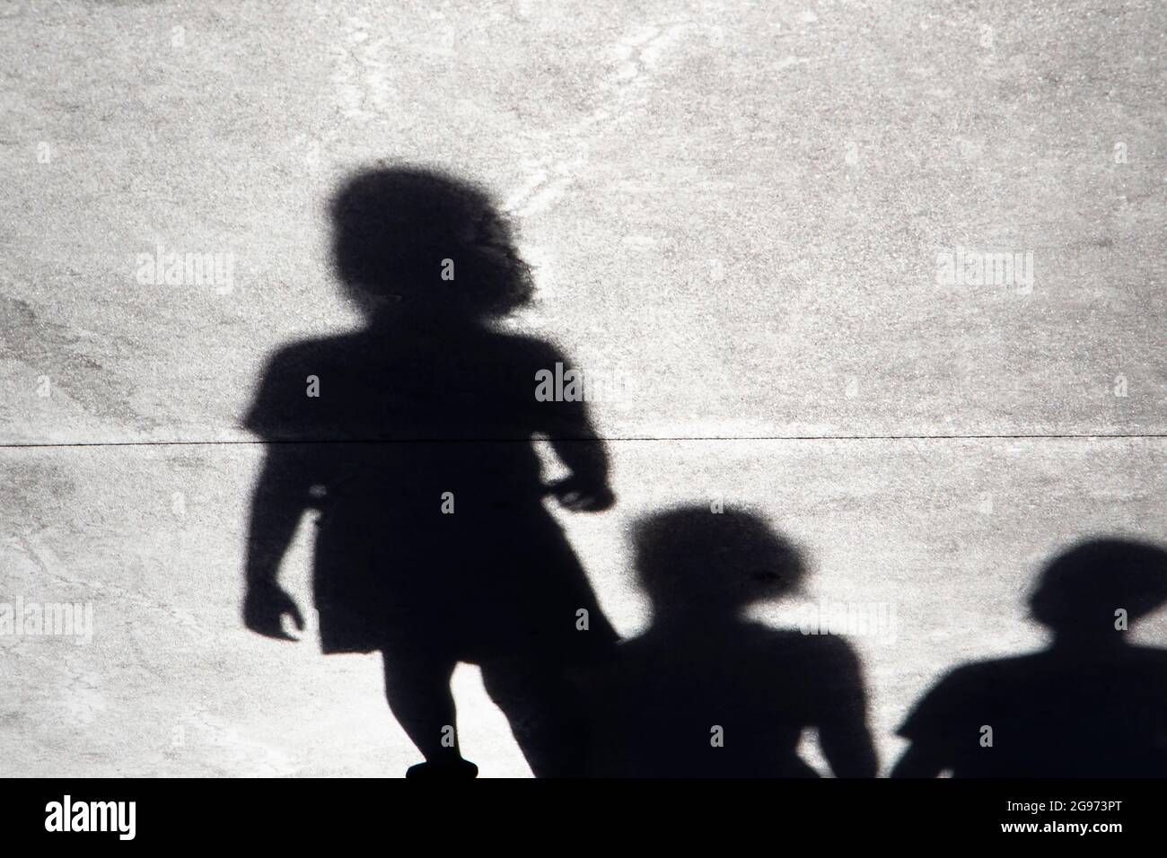 Silhouette ombra sfocata di una bambina che cammina da sola in una giornata estiva con una famiglia dietro di lei Foto Stock