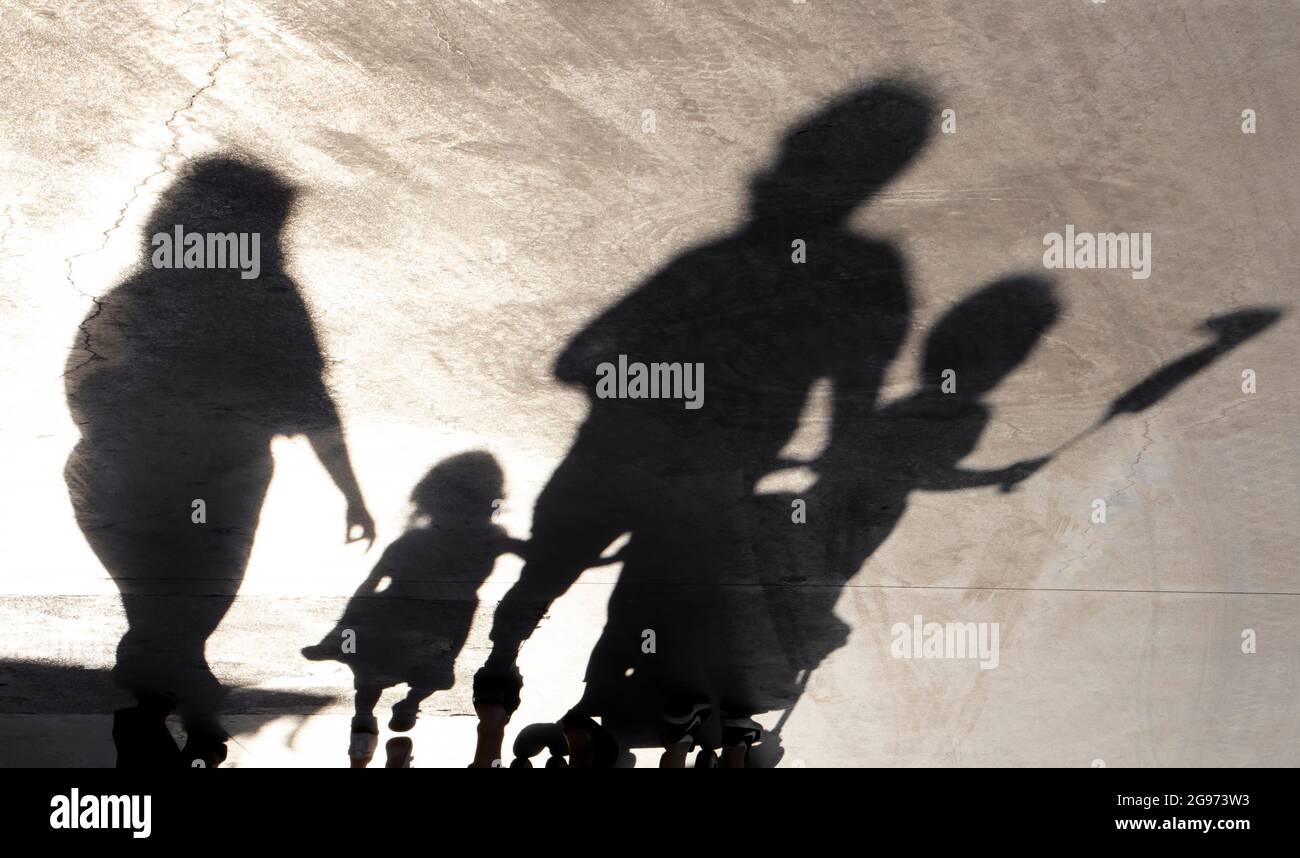 La silhouette oscurare di una famiglia con i bambini che camminano su una passeggiata in una giornata estiva Foto Stock