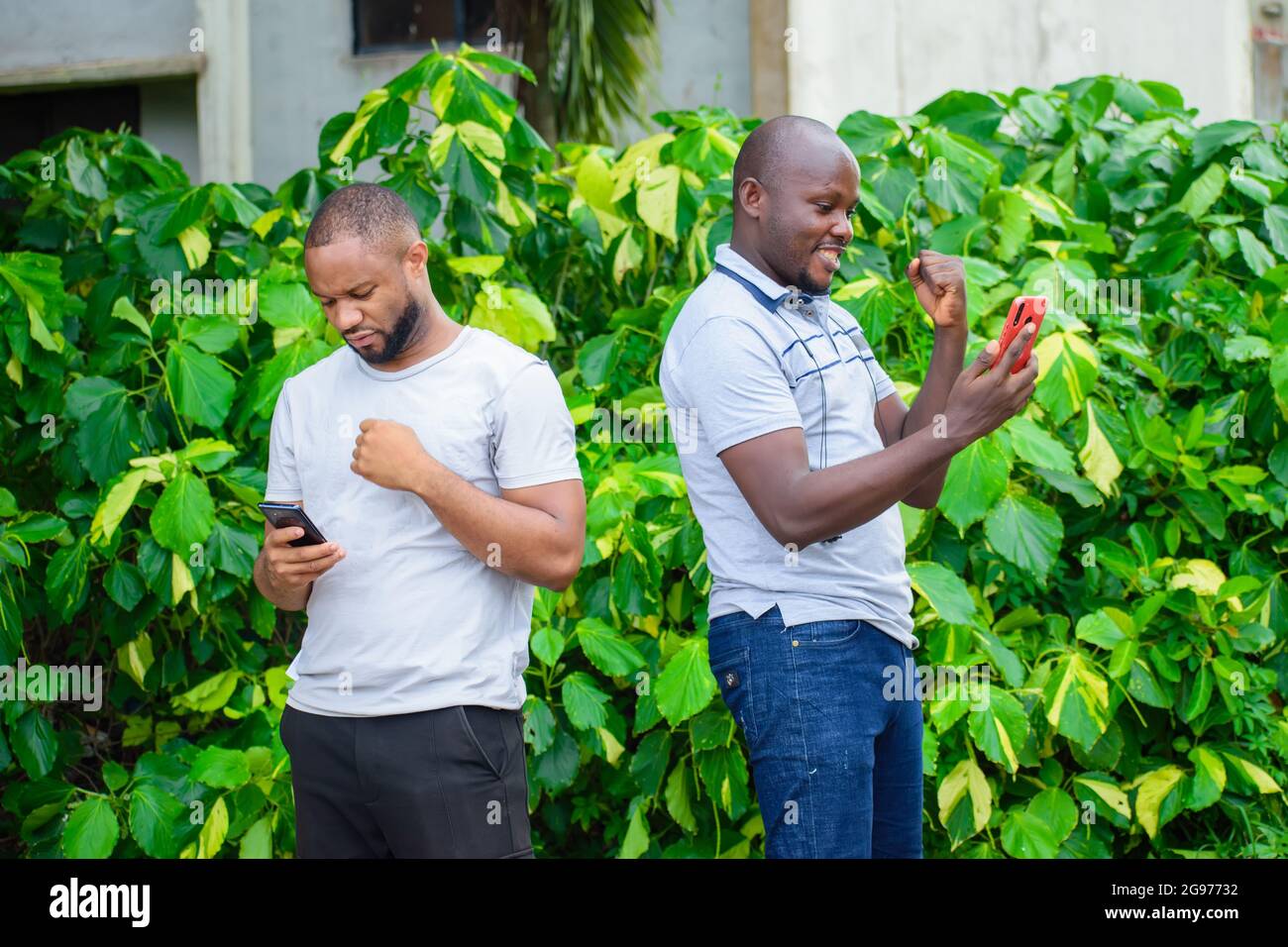 Due uomini o ragazzi africani che tengono smartphone con diverse espressioni riflessive e facciali Foto Stock