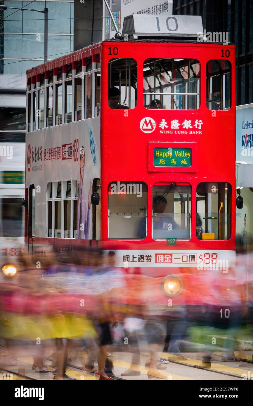 I pedoni attraversano Des Voeux Road, Central, Hong Kong Island, di fronte a un tram che aspetta a una luce rossa, con sfocatura selettiva del movimento Foto Stock