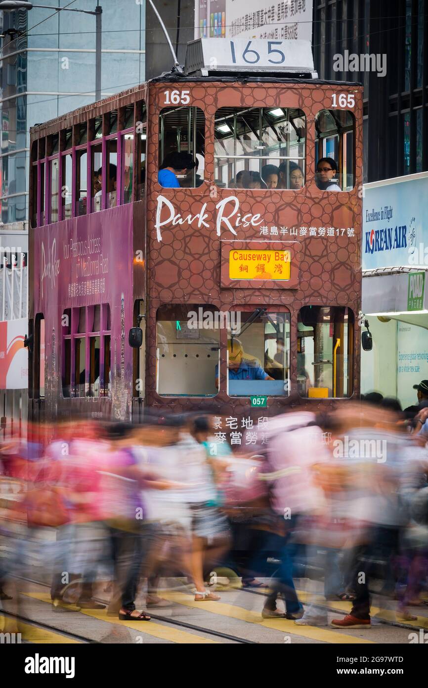 I pedoni attraversano Des Voeux Road, Central, Hong Kong Island, di fronte a un tram che aspetta a una luce rossa, con sfocatura selettiva del movimento Foto Stock