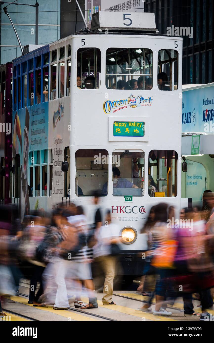 I pedoni attraversano Des Voeux Road, Central, Hong Kong Island, di fronte a un tram che aspetta a una luce rossa, con sfocatura selettiva del movimento Foto Stock