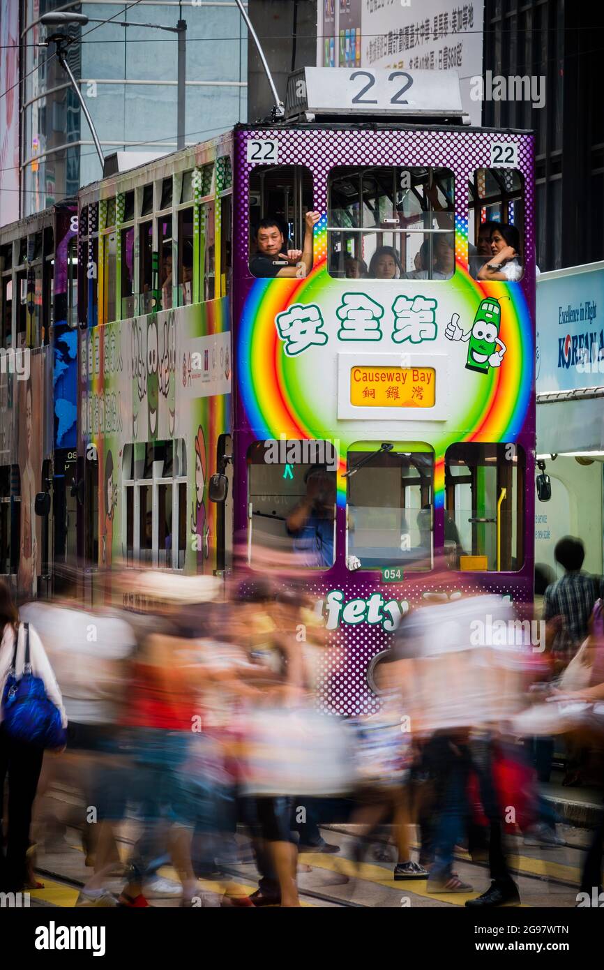 I pedoni attraversano Des Voeux Road, Central, Hong Kong Island, di fronte a un tram che aspetta a una luce rossa, con sfocatura selettiva del movimento Foto Stock