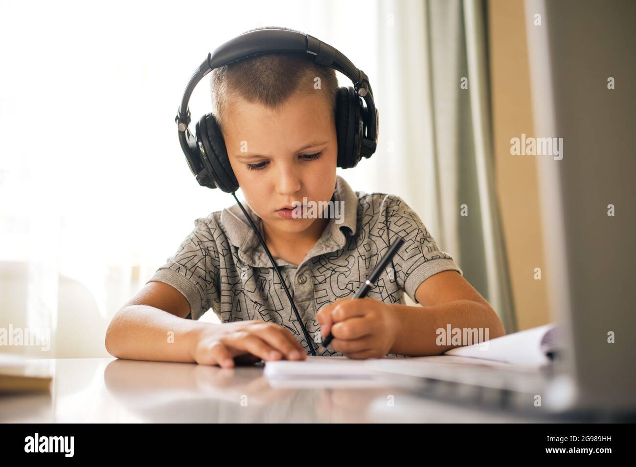 Ragazzo di scuola in cuffie scrivere in notebook e utilizzare il computer portatile durante la lezione online. Concetto di formazione online. Foto Stock