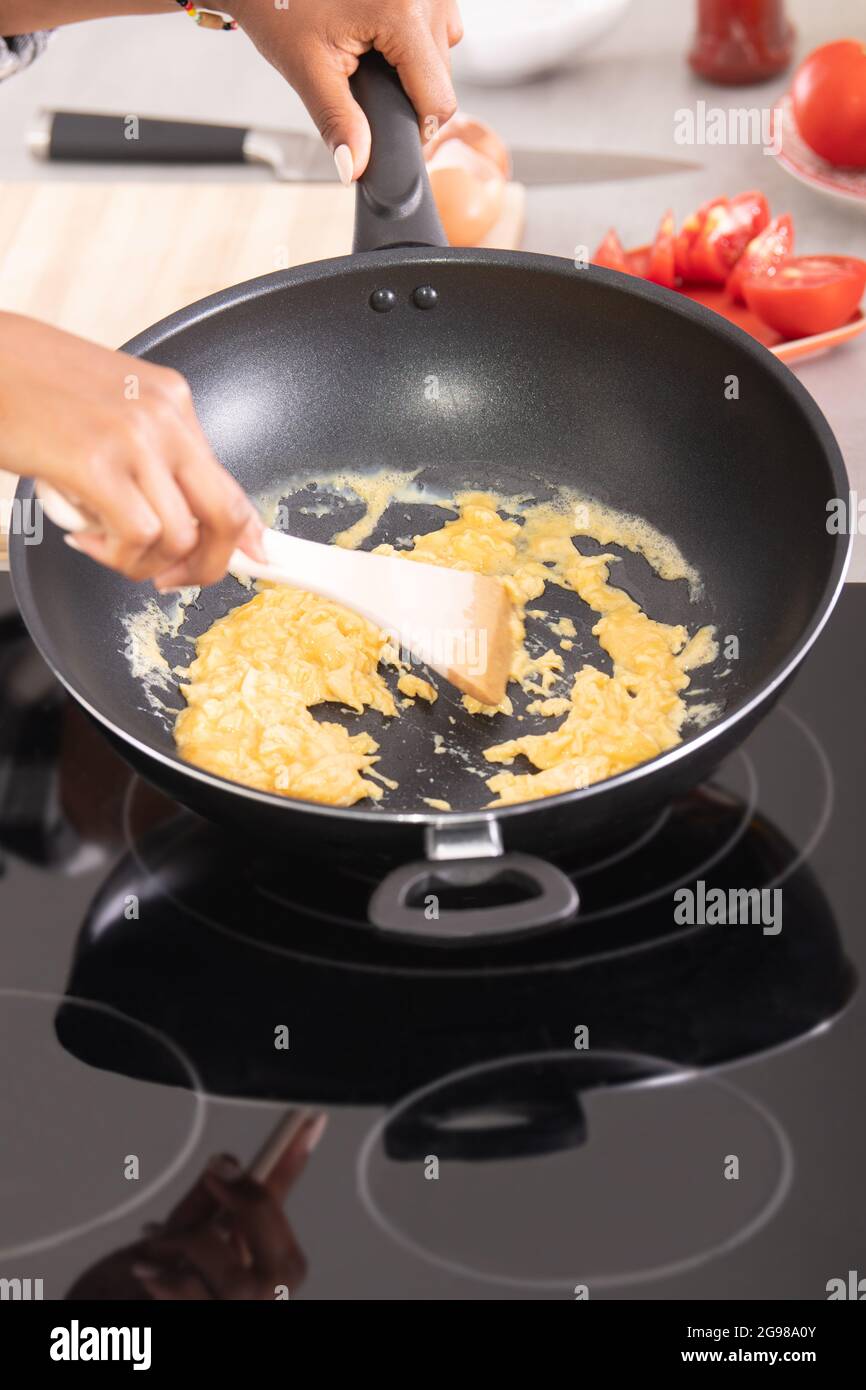 Ravvicinato le mani afro-americane che mescolano le uova su una padella profonda Foto Stock