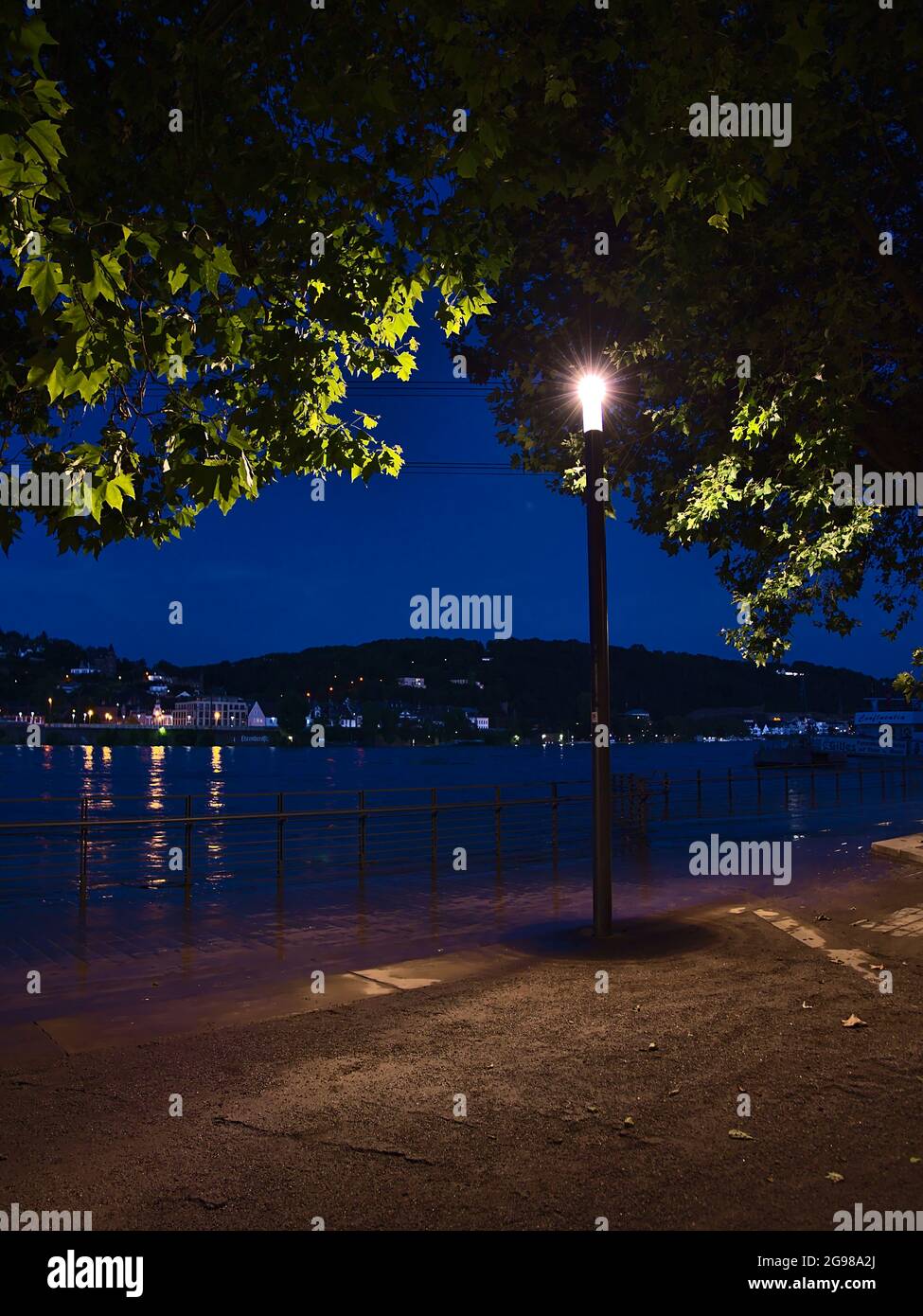 Vista notturna della passeggiata sul fiume Reno con alto livello dell'acqua illuminato da lanterna sotto l'albero nel centro di Coblenza. Foto Stock