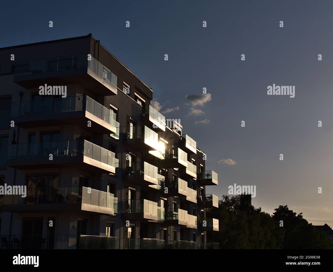 Vista di un moderno edificio residenziale multi-famiglia con appartamenti di lusso e il sole serale riflesso nelle ringhiere di vetro dei balconi. Foto Stock