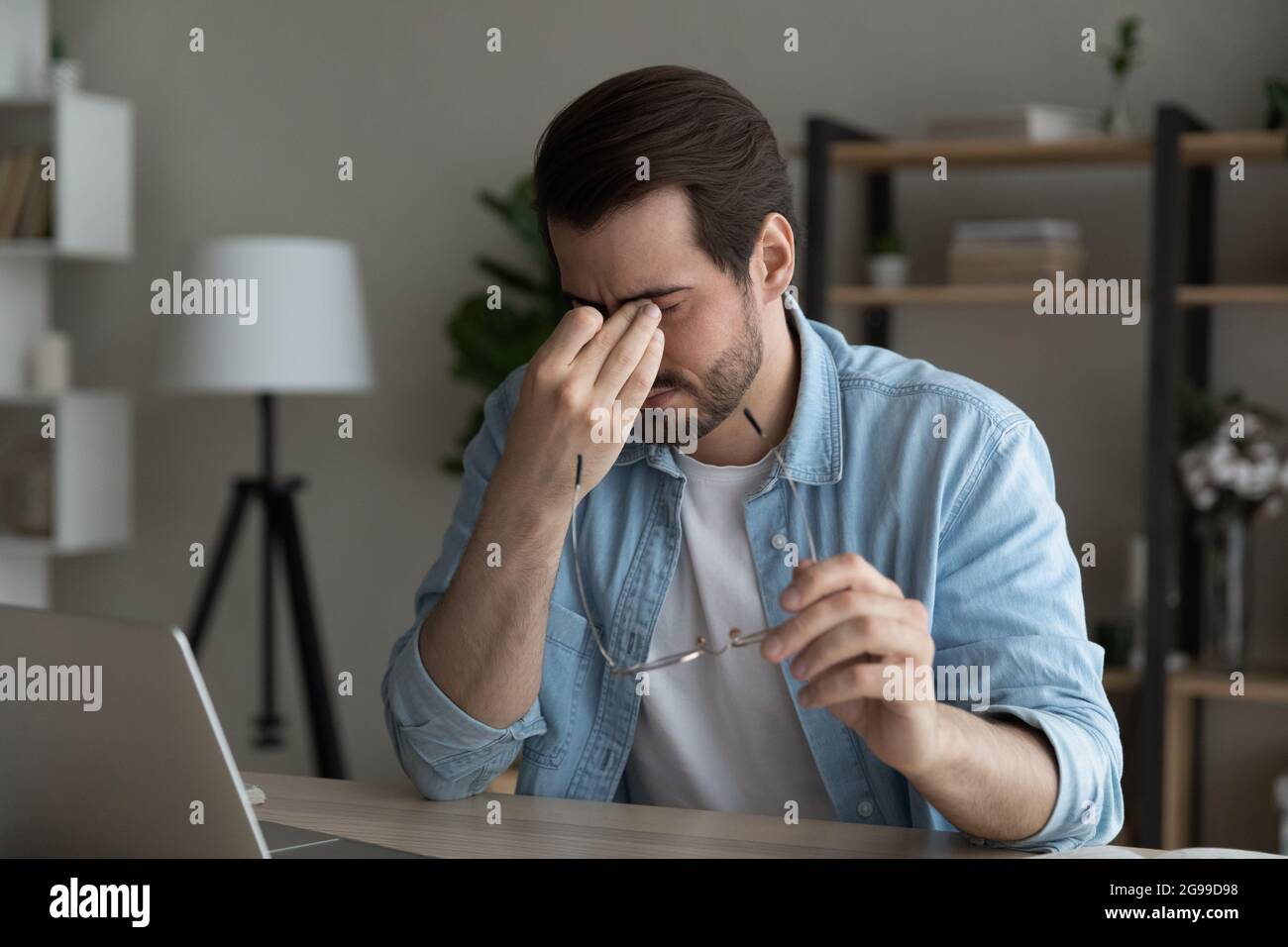 Uomo d'affari stanco dopo l'uso del laptop sensazione eyestrain toglie gli occhiali Foto Stock