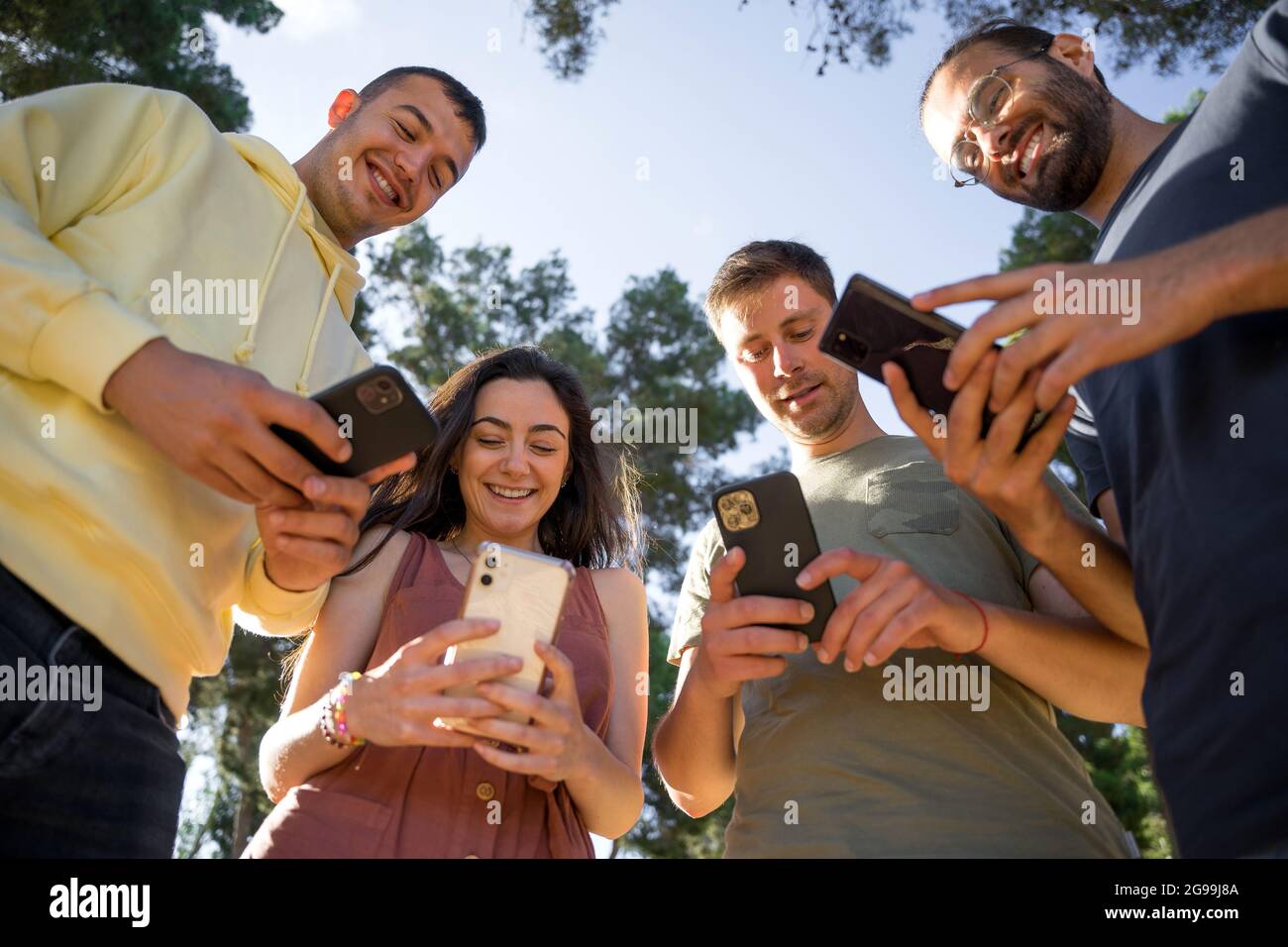 Amici sorridenti con i loro telefoni cellulari. Ognuno con il suo telefono cellulare. Sono caucasici e giovani. Indossano colorati abiti estivi. Clo Foto Stock