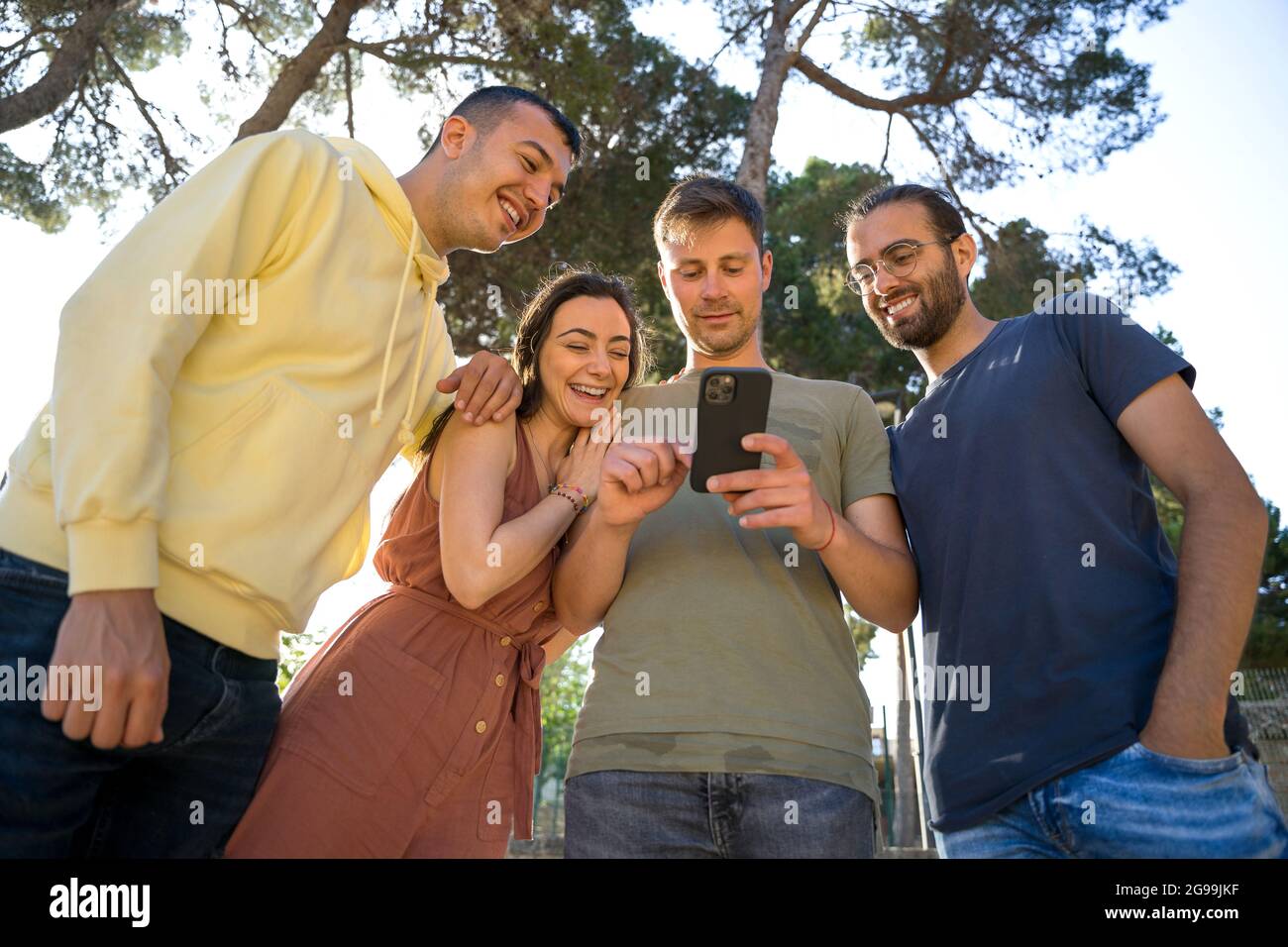 Amici sorridenti, stanno guardando lo stesso telefono cellulare. Sono caucasici e giovani. Indossano colorati abiti estivi. Primo piano. Th Foto Stock