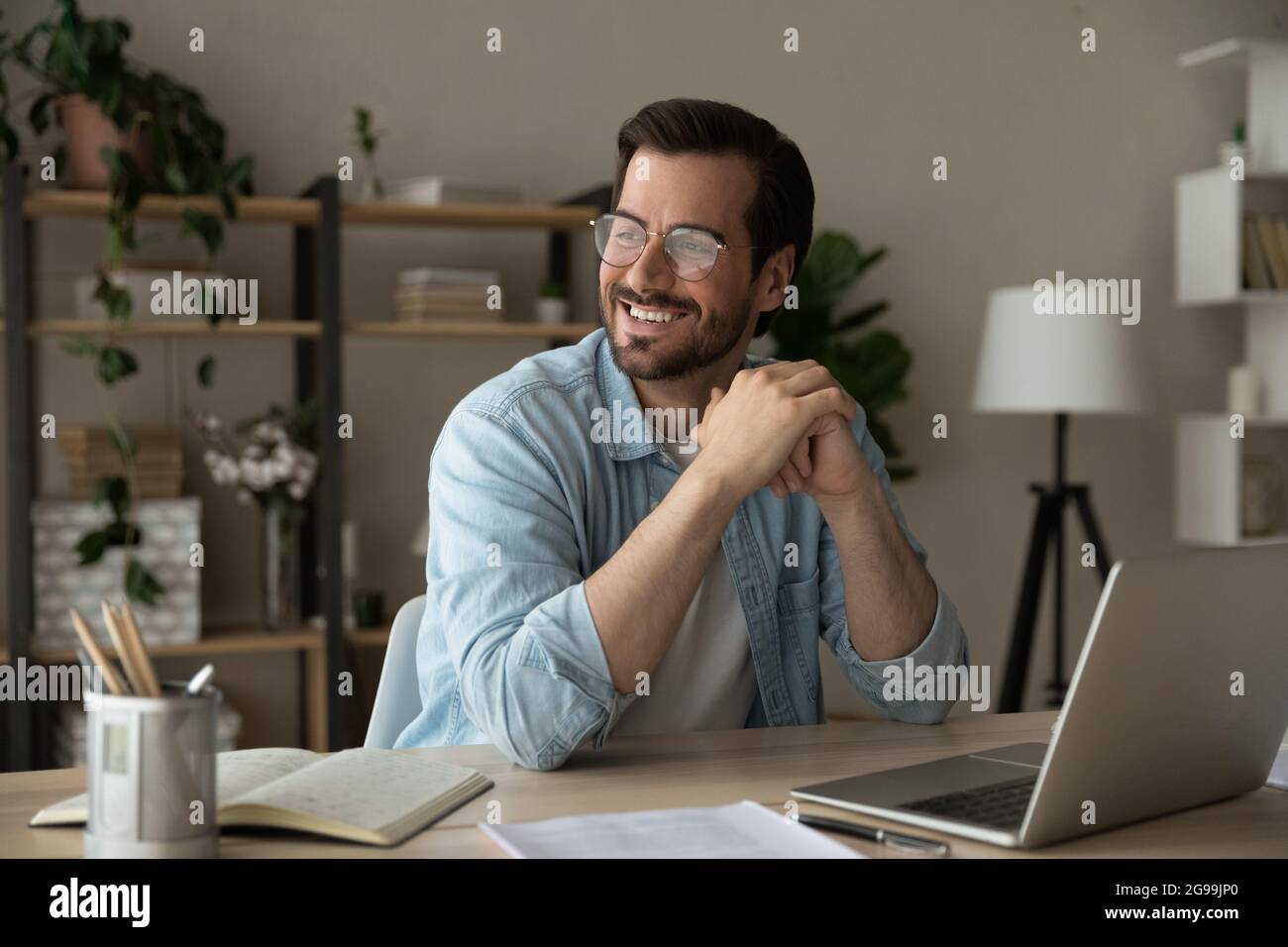 Un imprenditore sorridente di successo si siede alla scrivania guardando in lontananza Foto Stock