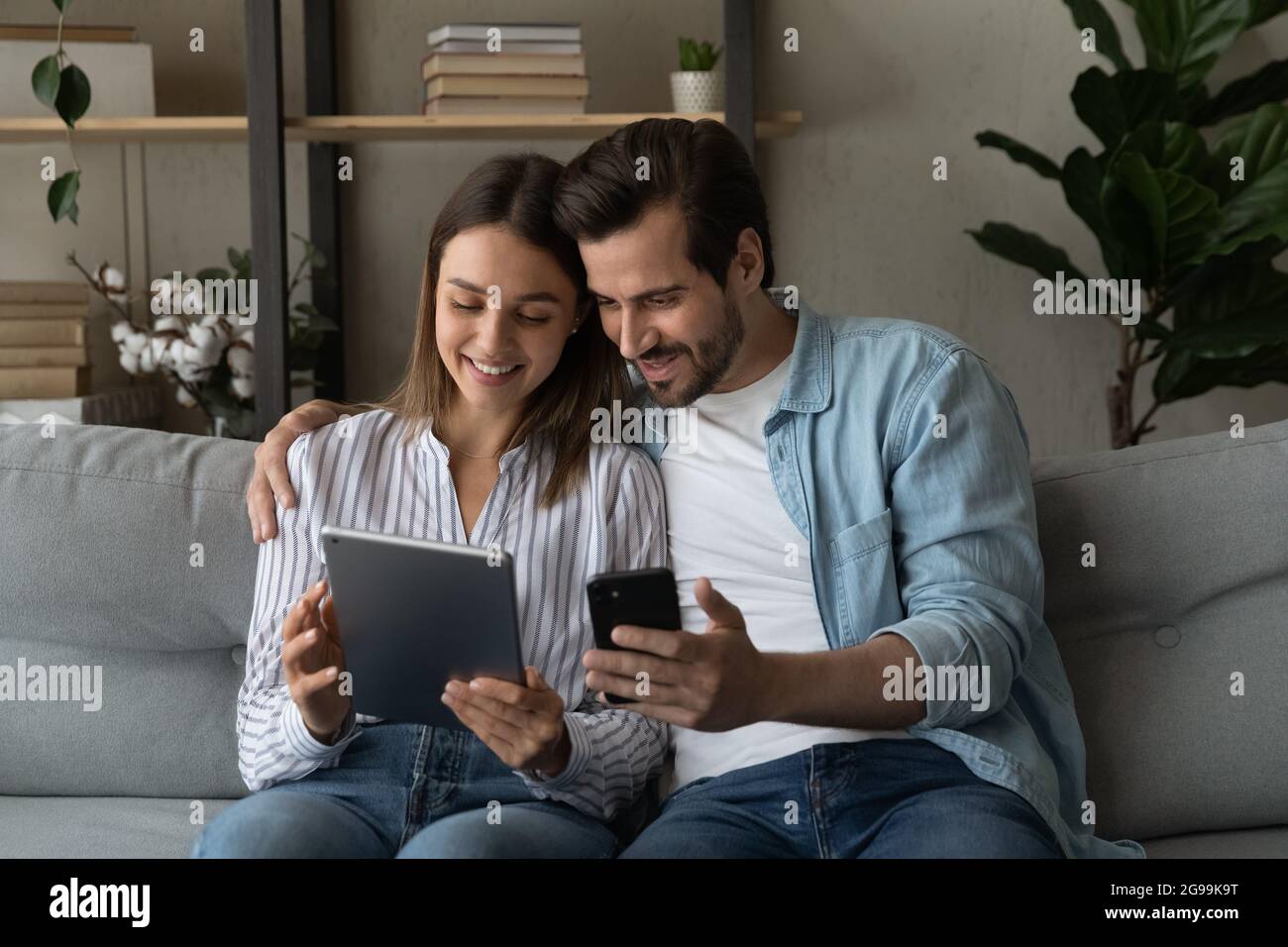 La coppia si siede sul divano con moderni gadget diversi Foto Stock