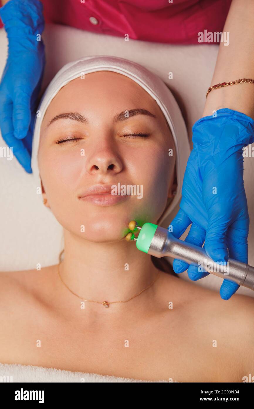 Giovane donna che ottiene la pulizia della pelle degli ultrasuoni e il trattamento del viso al salone di bellezza. Estetista si prende cura del suo viso Foto Stock