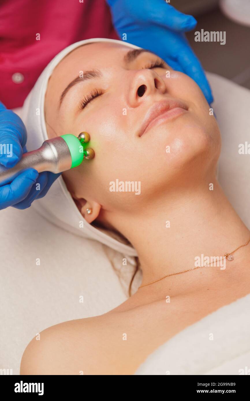 Giovane donna che ottiene la pulizia della pelle degli ultrasuoni e il trattamento del viso al salone di bellezza. Estetista si prende cura del suo viso Foto Stock