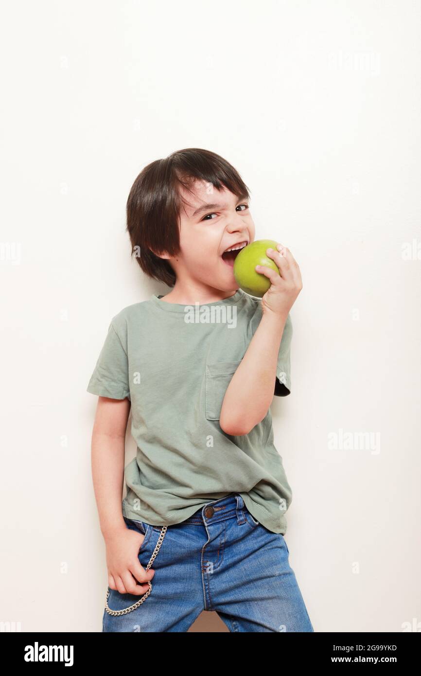 bambino su uno sfondo bianco mangiare una mela verde sulla macchina fotografica Foto Stock