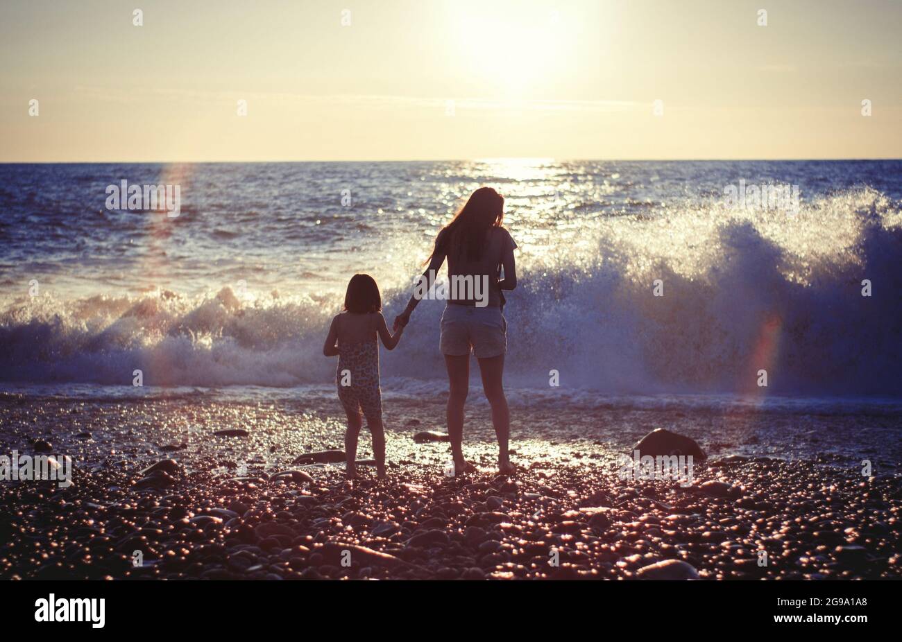 Madre con bambina sulla spiaggia del mare al tramonto Foto Stock