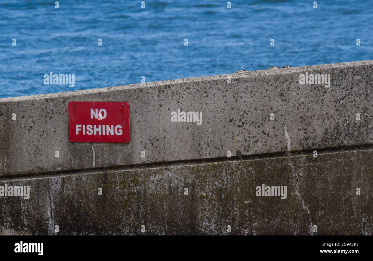 Cartello rosso No Fishing su parete di cemento con mare dietro Shell Beach Poole Dorset UK Foto Stock