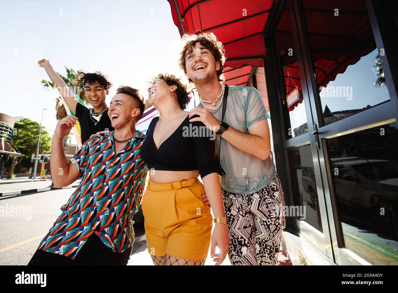 Felici i giovani LGBTQ+ che sfilano la bandiera dell'orgoglio arcobaleno all'aperto. Gruppo di giovani non conformi sorridendo allegro mentre teneva in mano l'arcobaleno Foto Stock