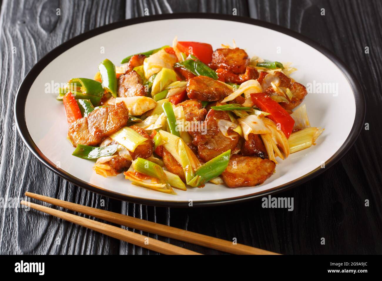 Il maiale cotto due volte è in stile Szechuan, pancia di maiale fritto in salsa e verdure in primo piano nel piatto sul tavolo di legno. Orizzontale Foto Stock