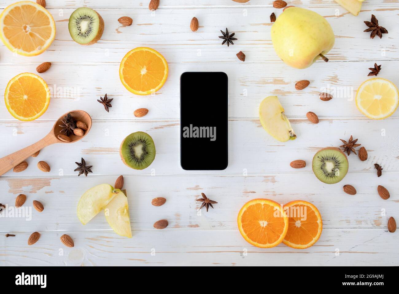 Concetto di alimentazione sana. Smartphone con schermo nero vuoto su tavolo di legno con fette di frutta, mandorla e anice stellato, vista dall'alto Foto Stock