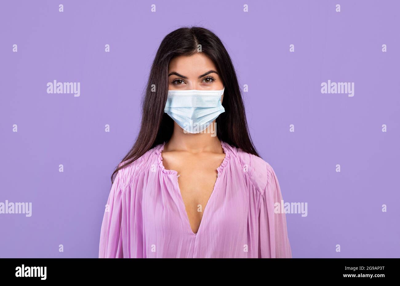 Concetto di protezione antivirus. Ritratto di donna armena in maschera medica protettiva sul viso su sfondo viola Foto Stock