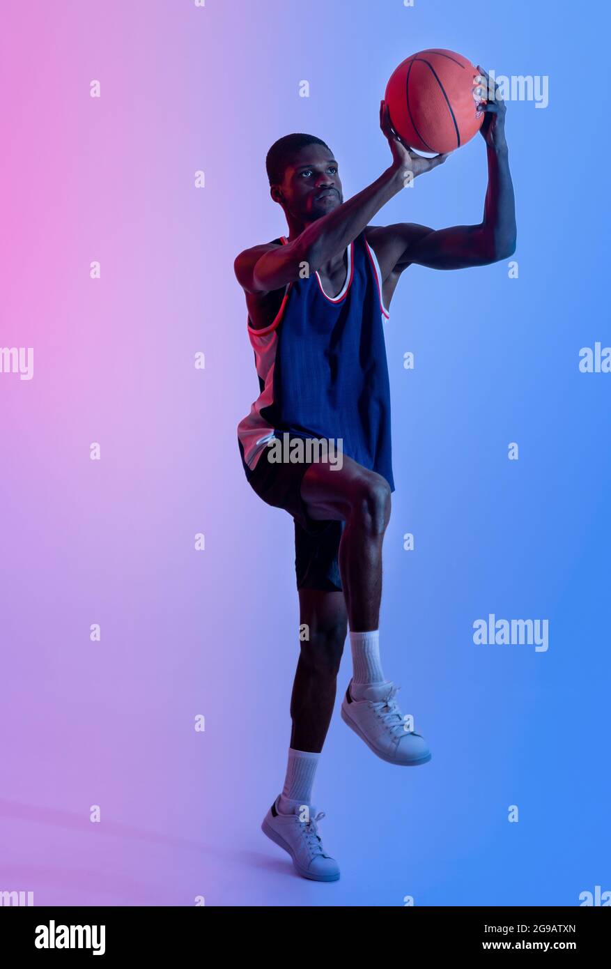 Lunghezza completa del giocatore professionista di pallacanestro afroamericano che salta e che segna la palla in luce del neon Foto Stock