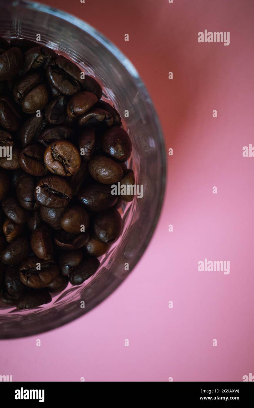 Chicchi di caffè in un bicchiere su sfondo rosa Foto Stock