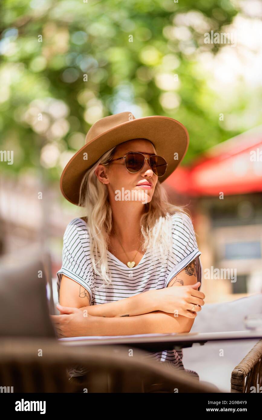Bella donna adulta di stile in un abbigliamento casual, cappello moderno e  occhiali da sole seduti al tavolo sulla terrazza del caffè. Look Street  fashion Foto stock - Alamy