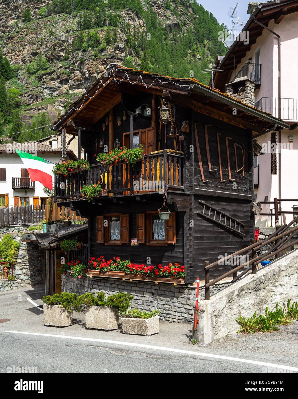 Una tipica casa in legno con fiori rossi e bandiera italiana in Valtournenche, Valle d'Aosta, Italia. Valtournenche, Italia, giugno 2021 Foto Stock