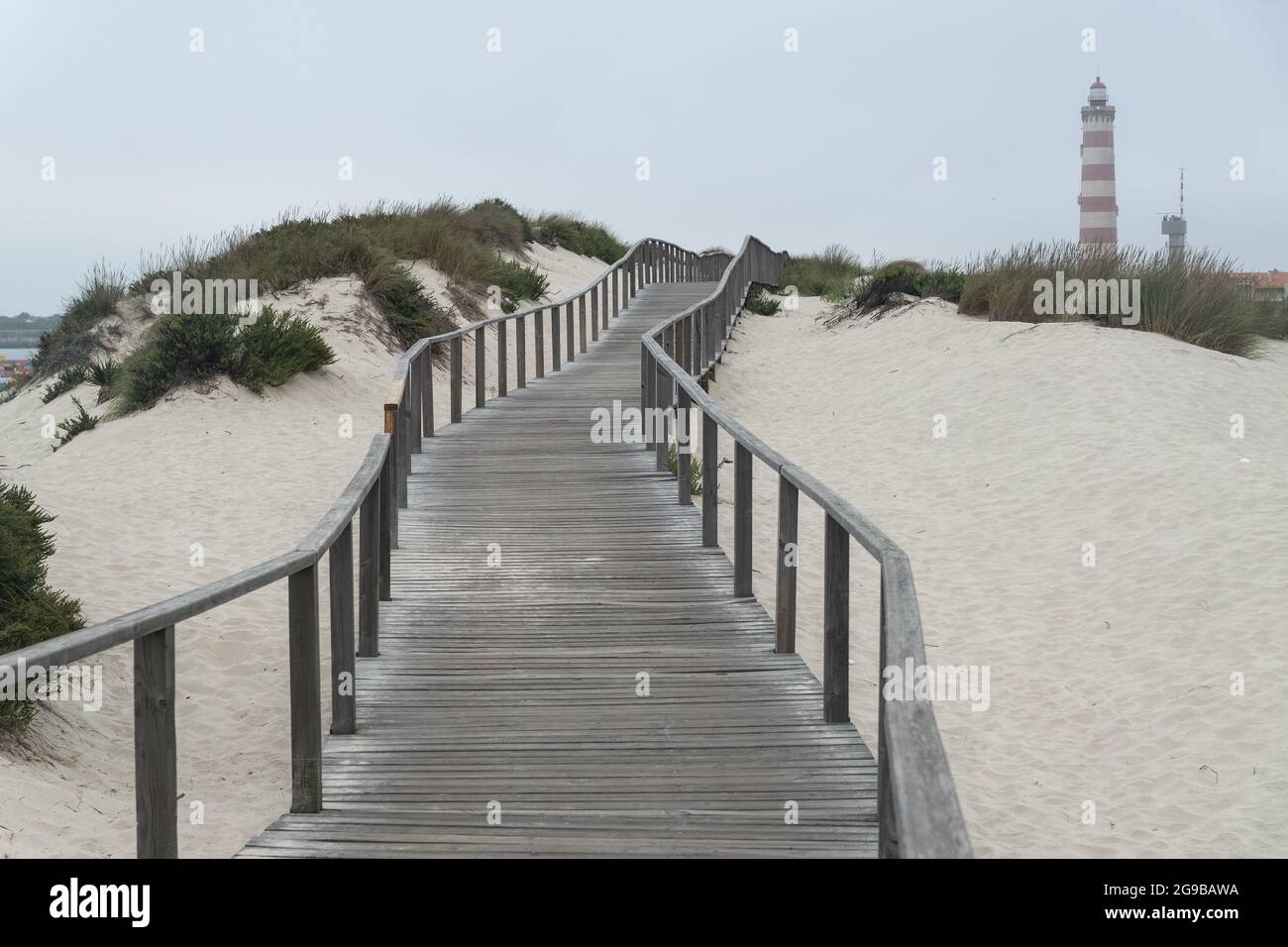 Passerelle in legno lungo le dune della spiaggia di barra con il faro di Aveiro sullo sfondo in una giornata nuvolosa. Portogallo Foto Stock