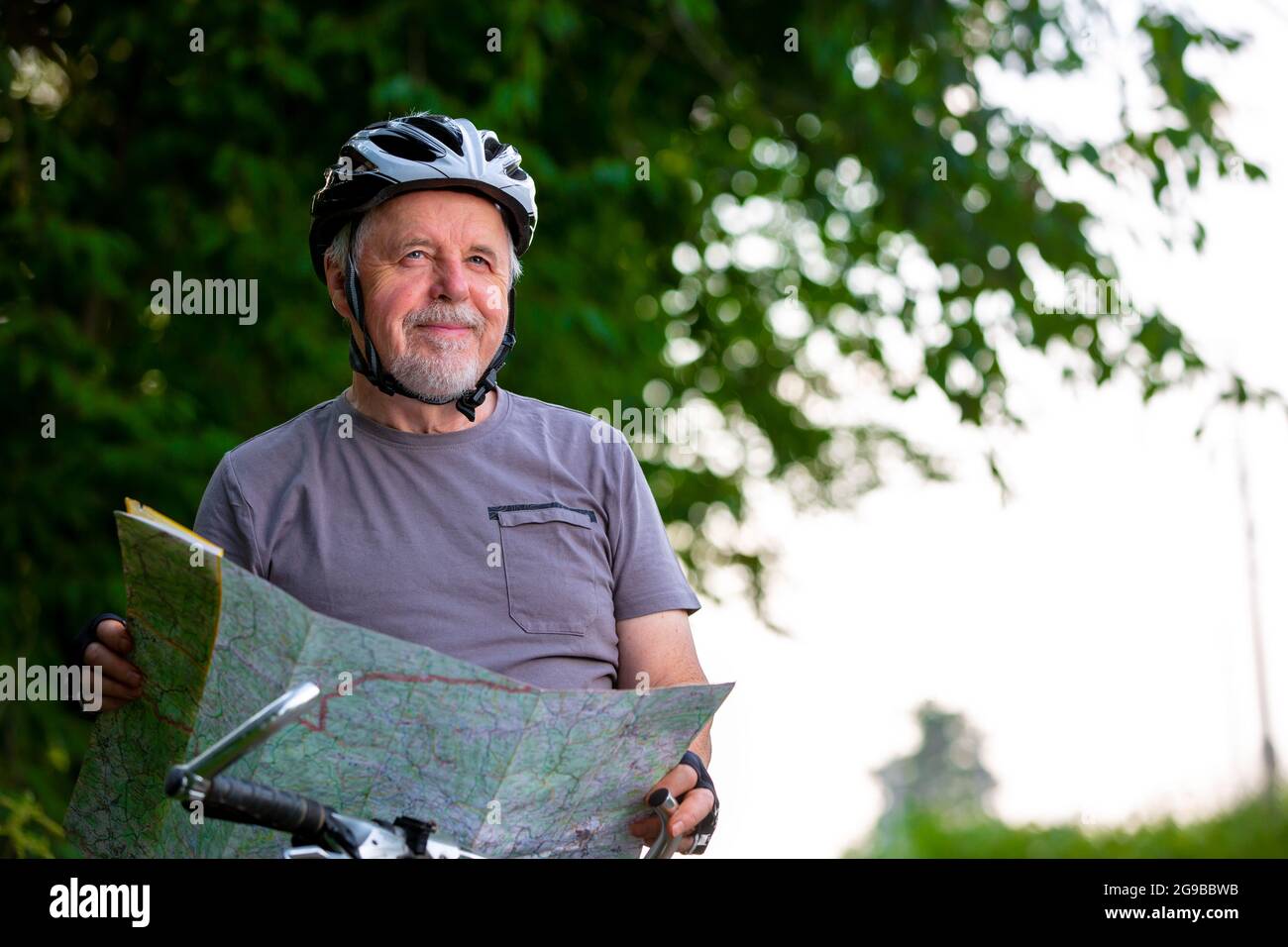 Sorridente uomo anziano attivo in bicicletta o in bicicletta fuori, scegliendo o selezionando il viaggio utilizzando la mappa, sano stile di vita concetto di sport Foto Stock