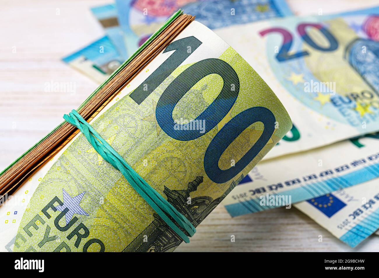 Rotolo di banconote da 100 euro contro un primo piano in valuta cartacea da 20 euro. Concetti di denaro, risparmio di denaro, contabilità di reddito e spese, conteggio di denaro Foto Stock
