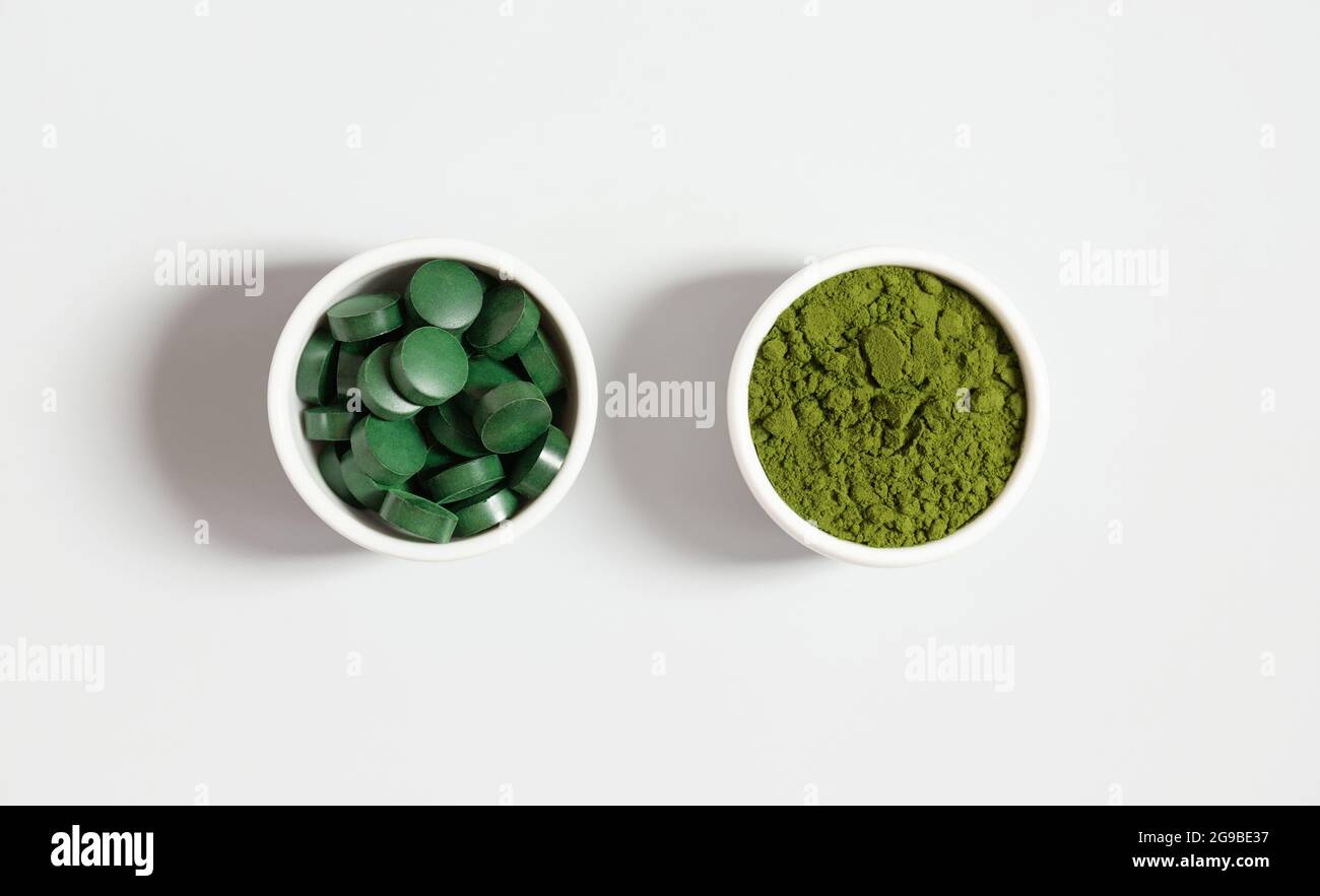 Clorella e spirulina. Pillole di Spirulina e polvere verde di clorella su sfondo bianco. Additivo alimentare minerale. Vista dall'alto. Foto Stock