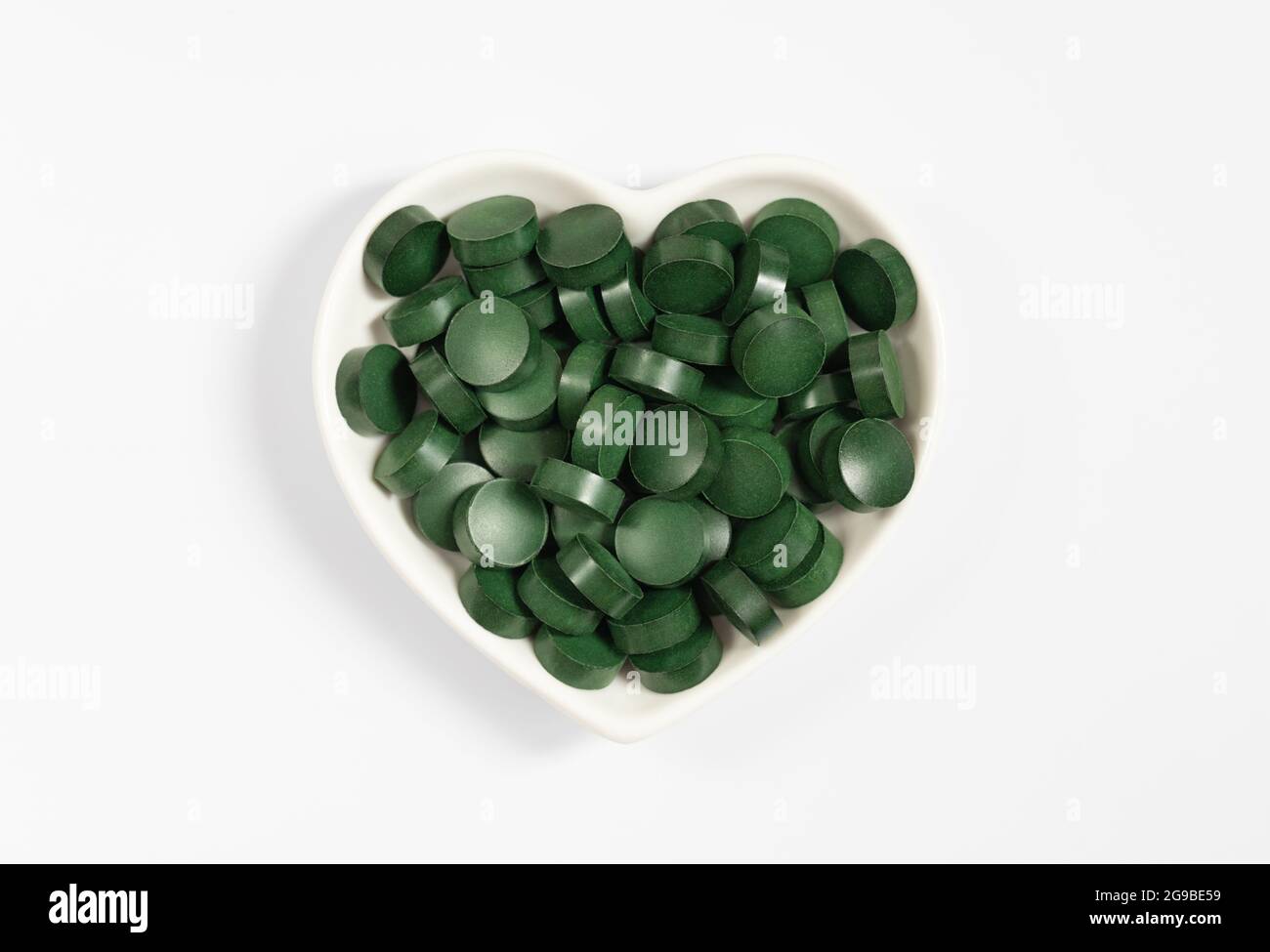 Spirulina pillole verdi in una piastra del cuore isolato su uno sfondo bianco. Supplemento naturale di alghe. Vista dall'alto. Foto Stock