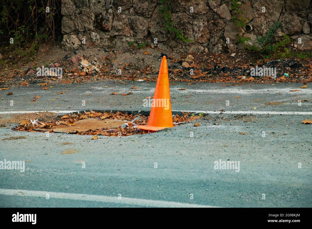 Emergenza cono arancione road pit scherma. La scherma riparazione su strada di asfalto distrutto. Buca su strada. Cono arancione su una strada di emergenza. Avviso di pericolo Foto Stock